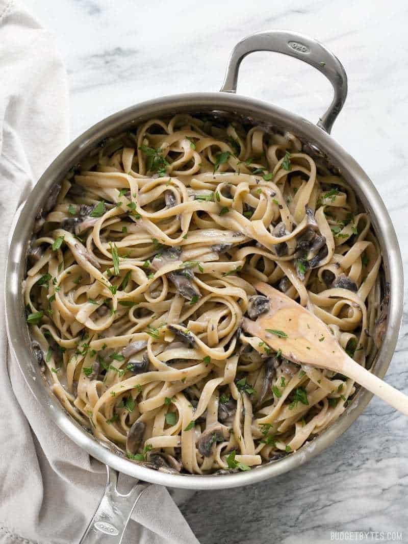 A skillet full of Creamy Mushroom Herb Pasta garnished with parsley and a wooden pasta fork in the side.