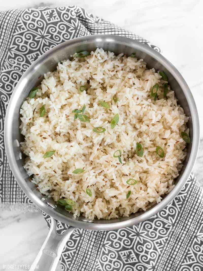 A pot of cumin rice garnished with sliced green onion, sitting on a patterned napkin.