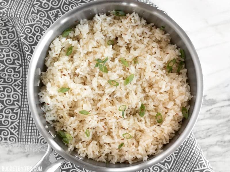 Cumin rice in a sauce pot garnished with sliced green onion sitting on a black and white patterned napkin.