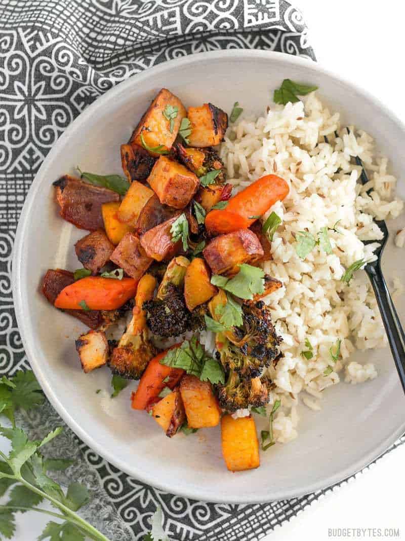 Close up of Harissa Roasted Vegetables in a bowl with cumin rice, on a black and white patterned napkin.