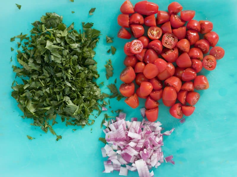 Chopped Parsley, Halved Tomatoes, Diced Onion on a cutting board