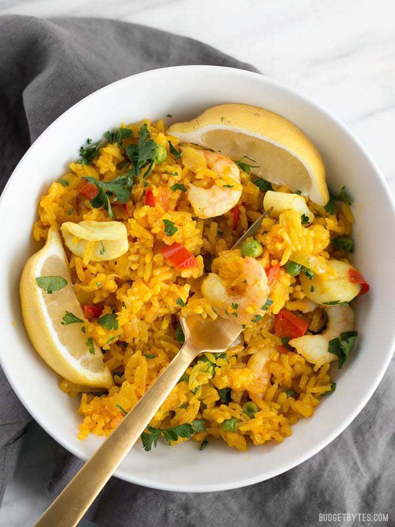 Close up of a bowl of Seafood Rice Skillet with a gold fork scooping a bite.