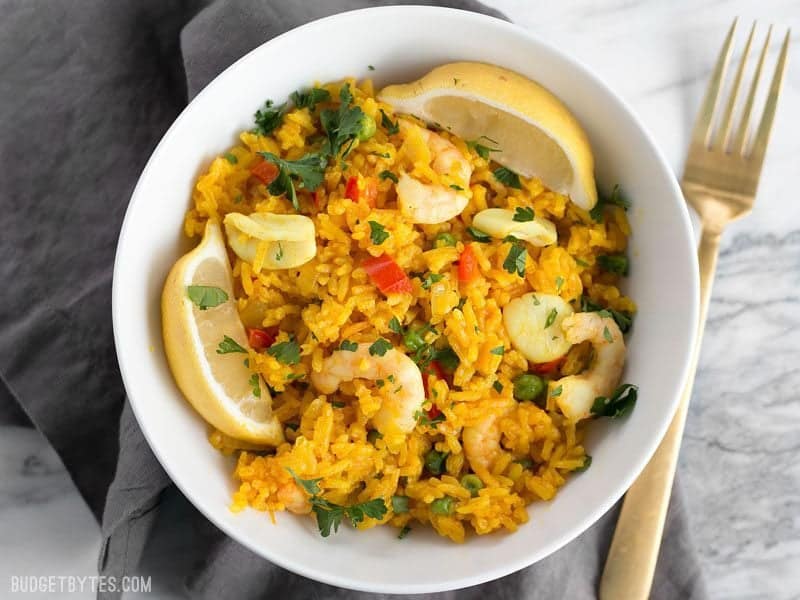 A bowl of Seafood Rice Skillet garnished with lemon wedges and parsley, a gold fork on the side