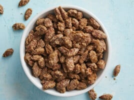 Overhead view of candied almonds in a bowl on a blue background.