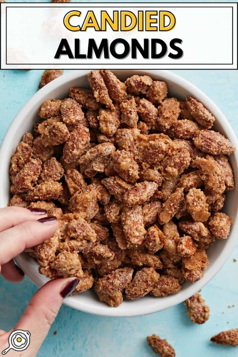 Overhead view of a bowl full of candied almonds with a hand grabbing a few.