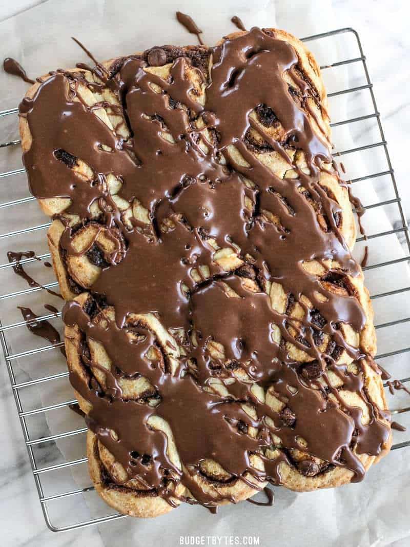 12 chocolate cinnamon buns drizzled with chocolate icing, cooling on a wire cooling rack