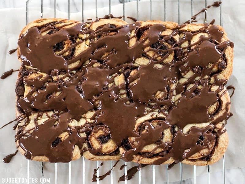 12 chocolate cinnamon buns drizzled with chocolate glaze, cooling on a wire rack