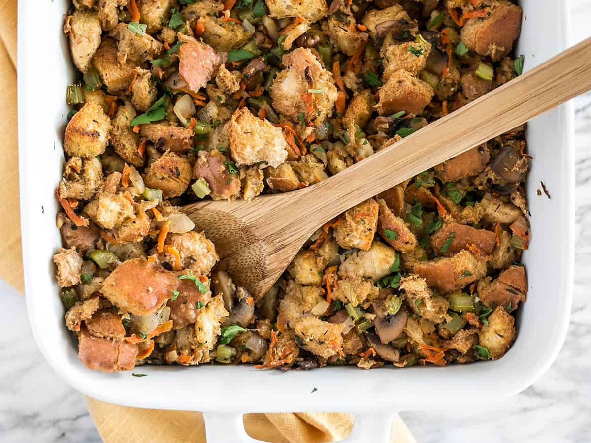 Overhead view of vegetarian stuffing in the casserole dish with a wooden spoon. 