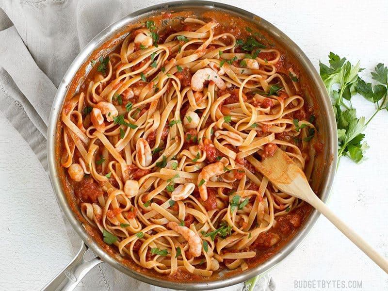 Spicy Seafood Pasta with Tomato Butter Sauce in the skillet with a wooden pasta fork and parsley on the side