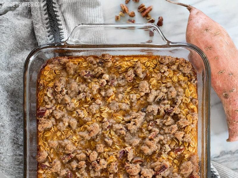 Finished Sweet Potato Casserole Baked Oatmeal in the glass casserole dish sitting on a napkin with a whole sweet potato and pecans on the side