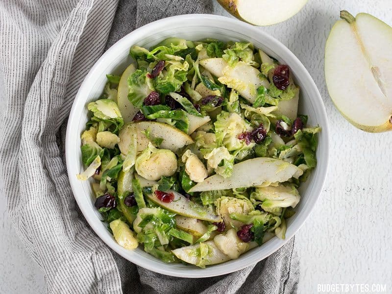 Overhead shot of Warm Brussels Sprouts and Pear Salad in the bowl, a fresh pear on the side