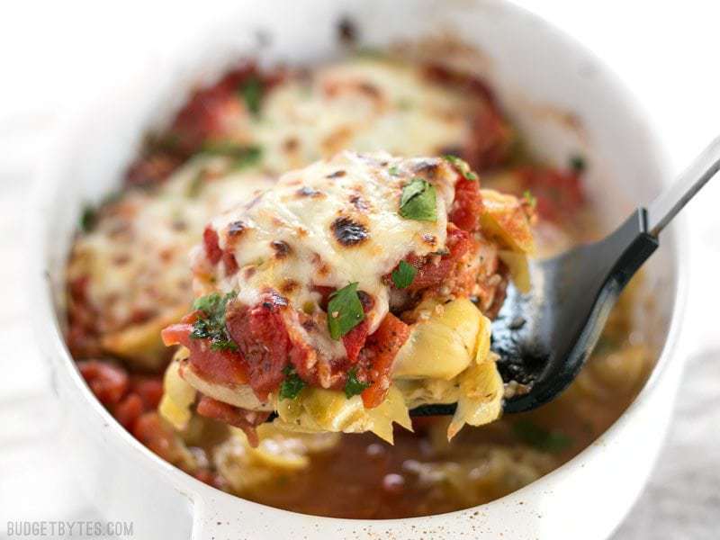 A piece of Baked Chicken with Artichokes and Tomatoes being lifted out of the casserole dish with a spatula