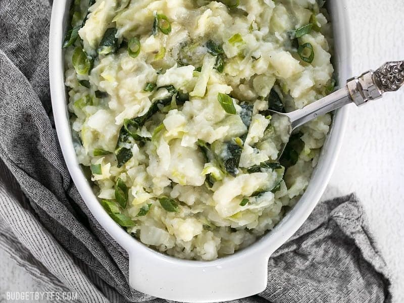 Overhead view of half of the casserole dish full of Colcannon with a big spoon digging in.