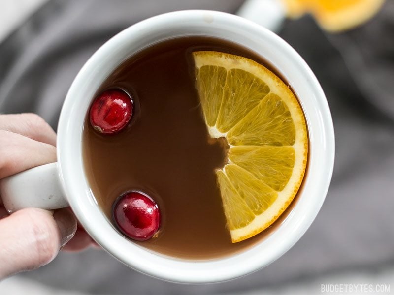 Close up of a mug full of Slow Cooker Spiced Cranberry Apple Cider with cranberries and an orange slice floating on top