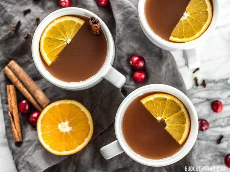 Three mugs of Slow Cooker Spiced Cranberry Apple Cider with garnishes, viewed from above