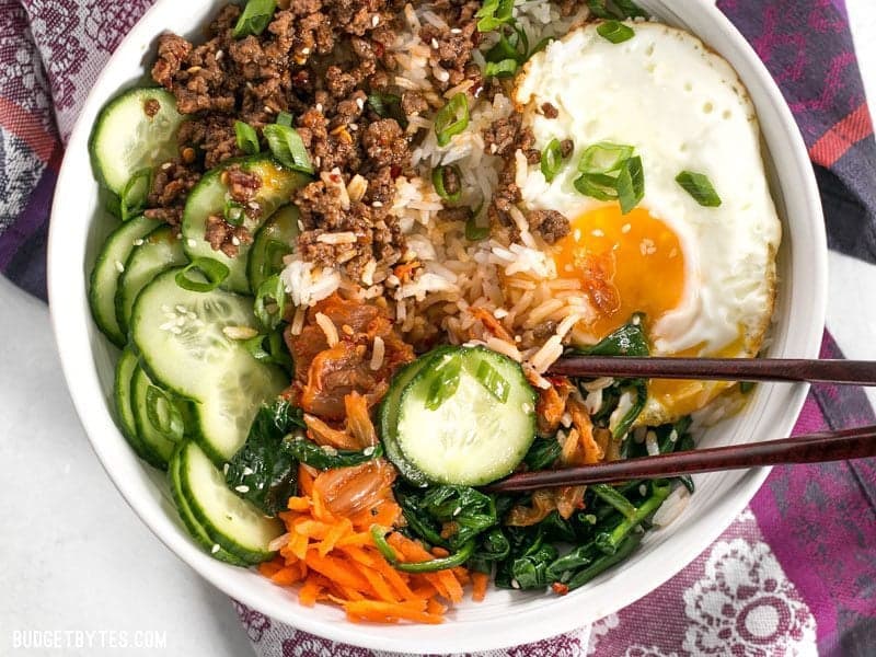 Bird's eye view of a bowl of Bibimbap being eaten with chopsticks. 