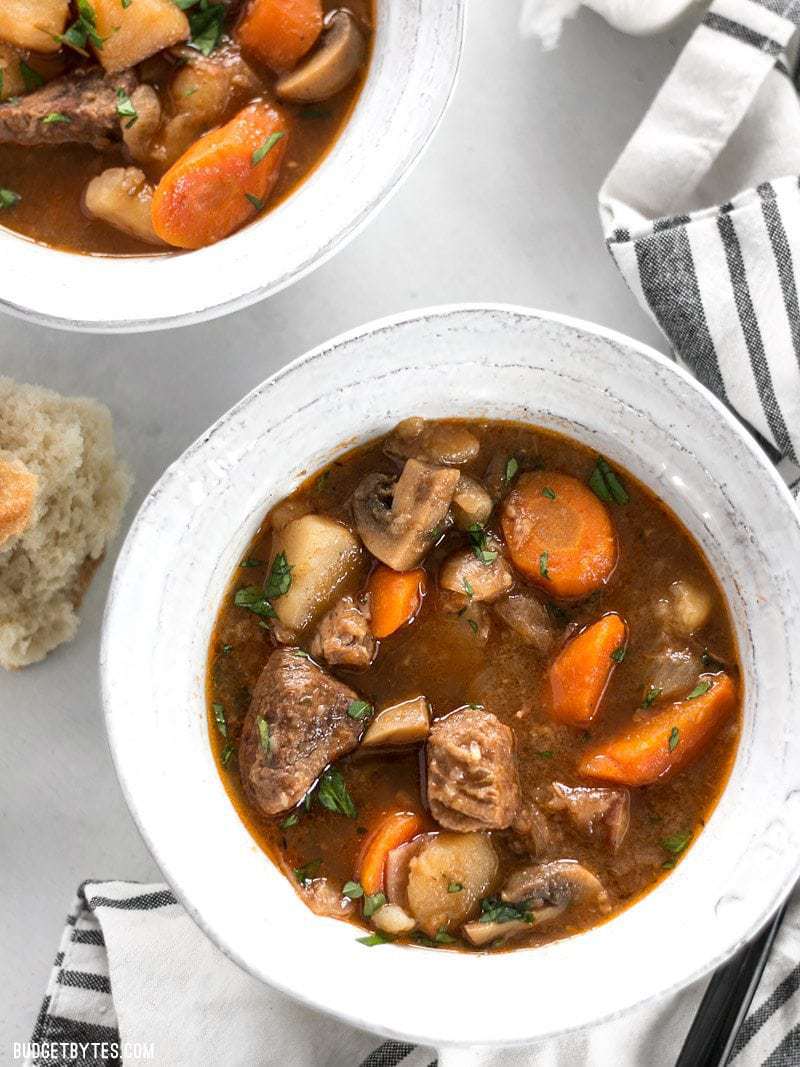 Two bowls of Instant Pot Beef Stew garnished with parsley, next to a striped napkin