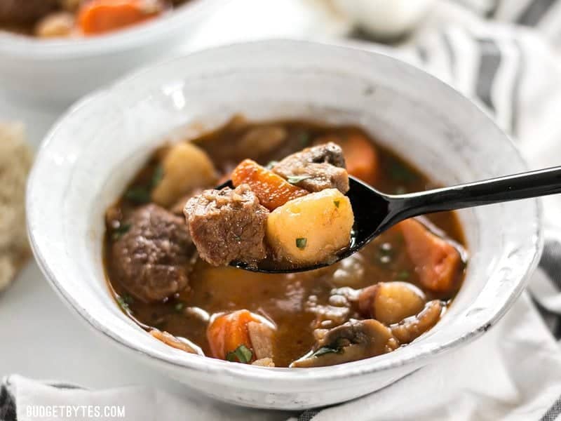 Close up of a spoonful of Instant Pot Beef Stew with the bowl in the background