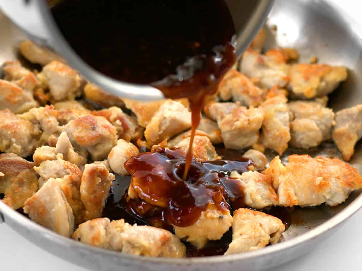 Close up of orange sauce being poured over the chicken pieces in the skillet.