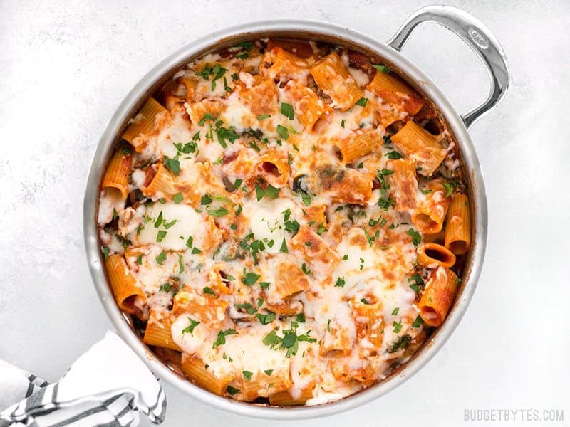 Finished Cheesy Rigatoni Skillet garnished with parsley, a towel wrapped around the handle of the skillet