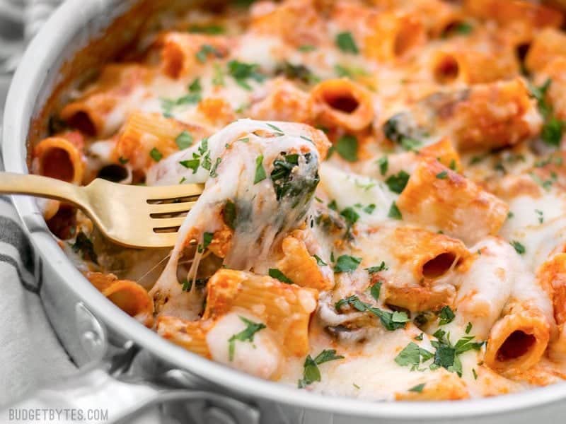 Close up of a fork pulling a cheesy bite of Cheesy Rigatoni out of the skillet