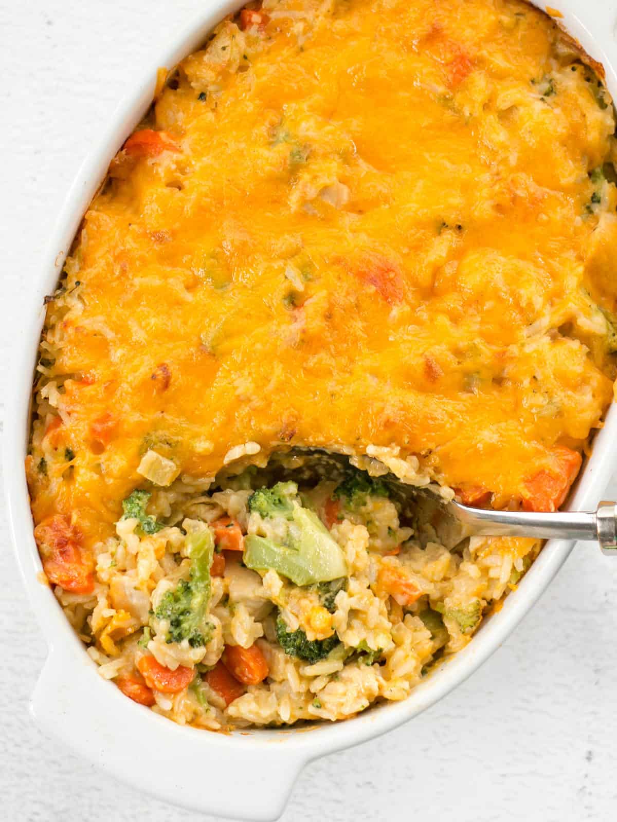 Overhead view of cheesy chicken and rice casserole being scooped out of the dish.