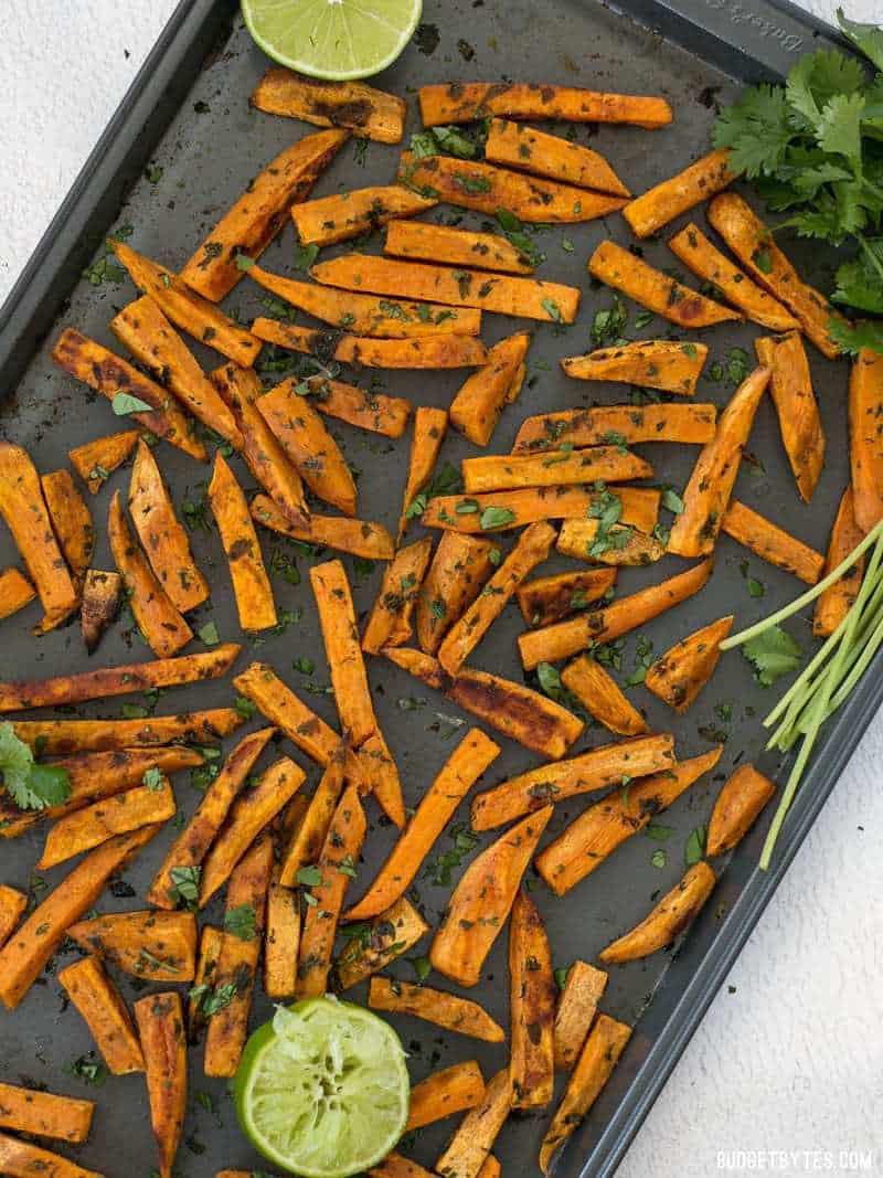 Overhead view of Cumin Lime Roasted Sweet Potatoes on the baking sheet with limes and cilantro