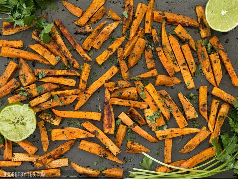 Finished Cumin Lime Roasted Sweet Potatoes on the baking sheet with cilantro and limes