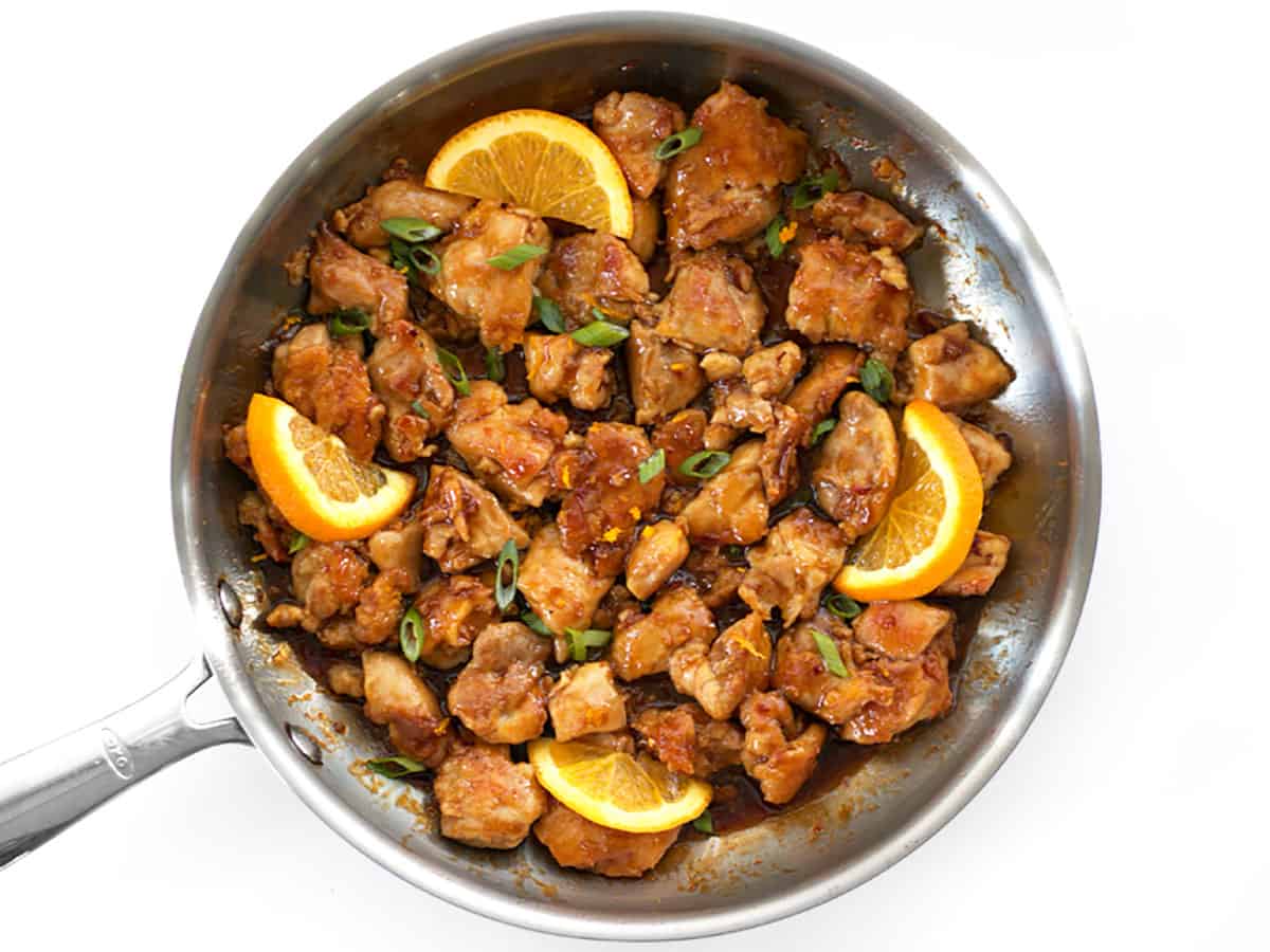 Finished orange chicken in the skillet with green onion and orange slices. 