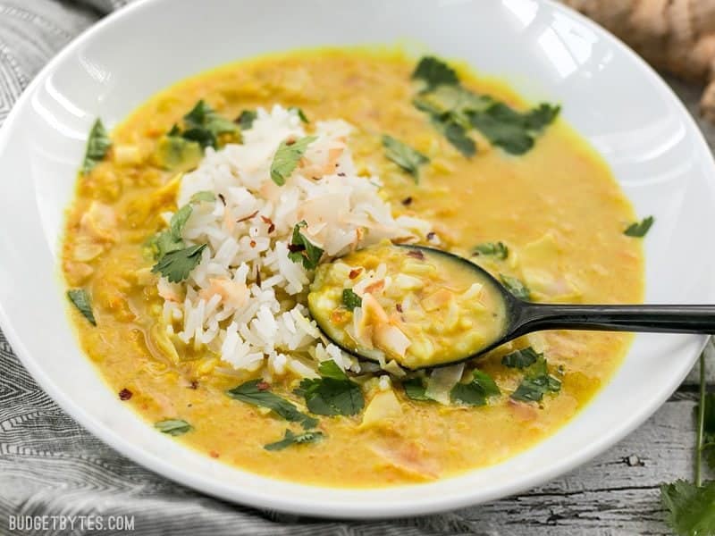 Front view of a bowl of Golden Coconut Lentil Soup with rice, coconut flakes, and cilantro garnishes