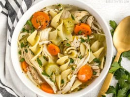 Close up overhead view of a bowl of homemade chicken noodle soup with a gold spoon on the side.