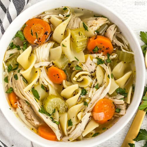 Close up overhead view of a bowl of homemade chicken noodle soup with a gold spoon on the side.