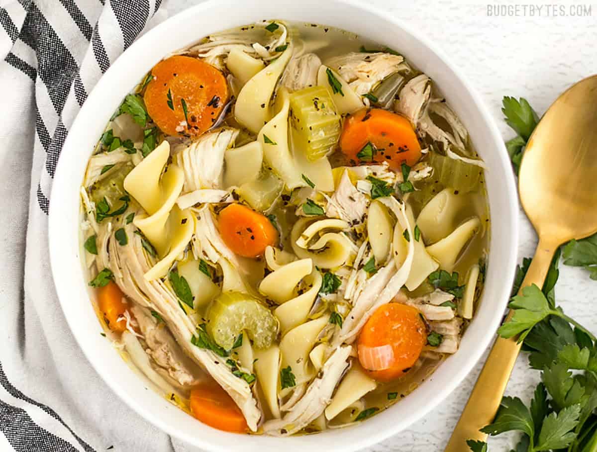 Close up overhead view of a bowl of homemade chicken noodle soup with a gold spoon on the side.