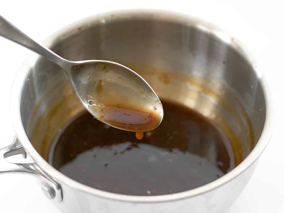 Orange sauce dripping off a spoon into a sauce pot full of sauce.