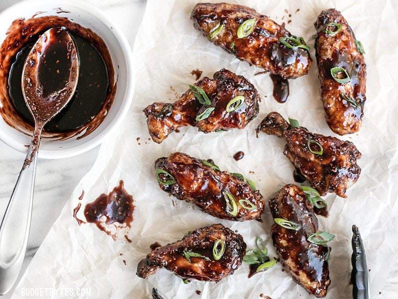 Raspberry Balsamic Baked Chicken Wings on parchment next to a bowl of balsamic sauce with a spoon