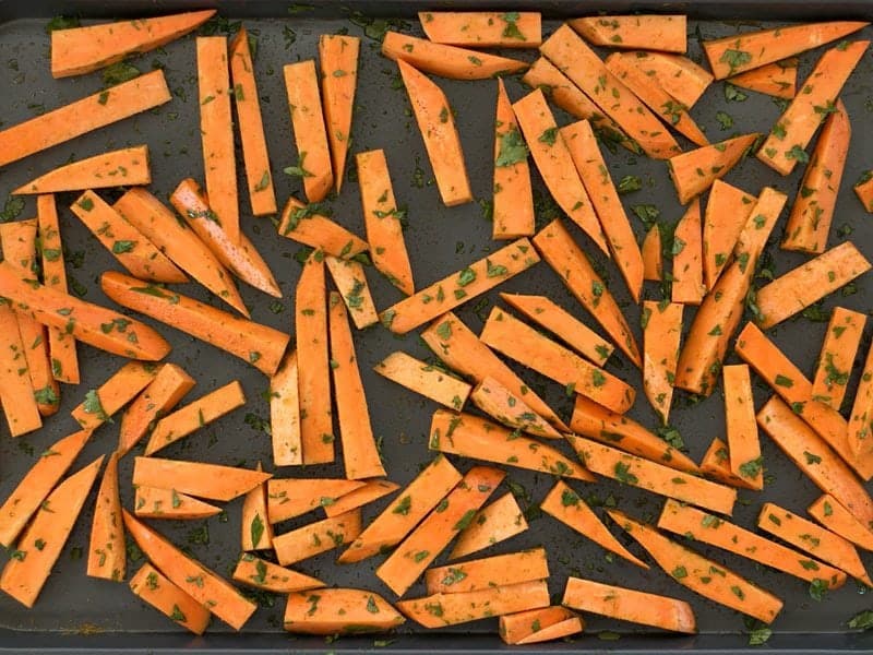 Seasoned Sweet Potatoes cut into fries, on the baking sheet