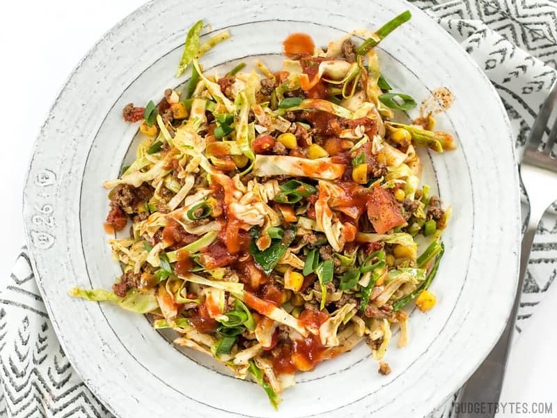 A white plate full of Southwest Beef and Cabbage Stir Fry with taco sauce drizzled over top