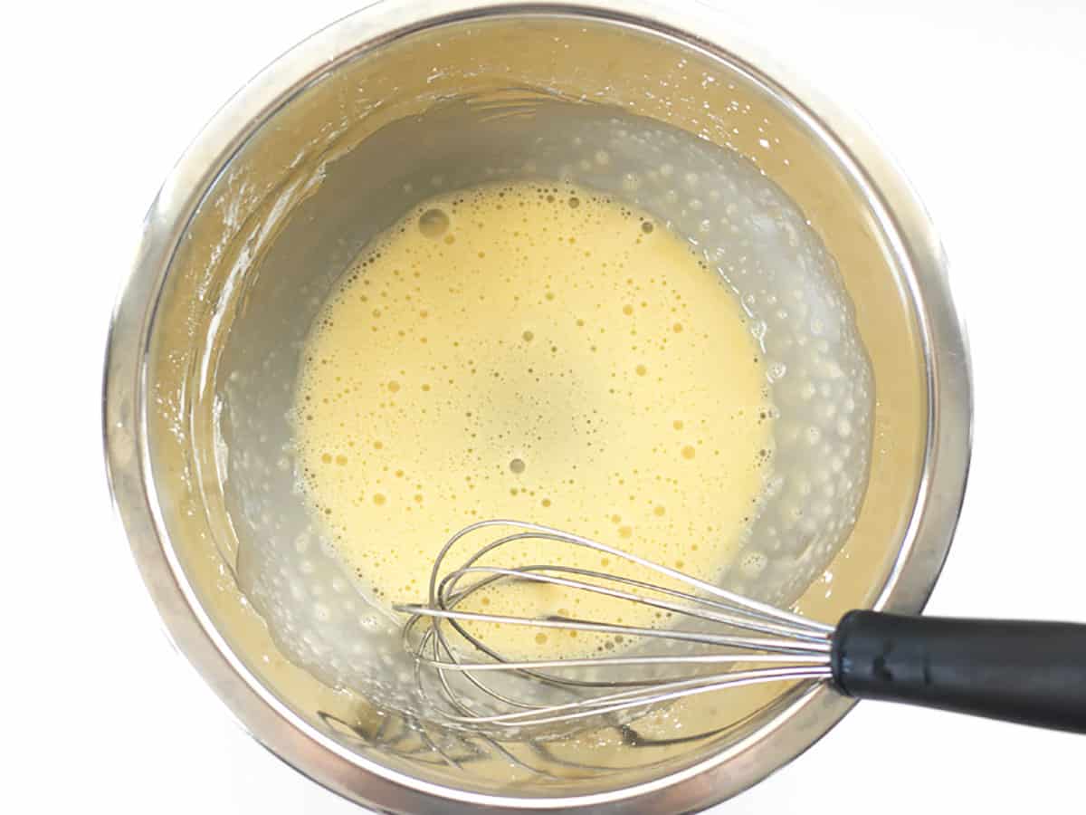 Whisked cornstarch and egg in a metal bowl with a whisk.