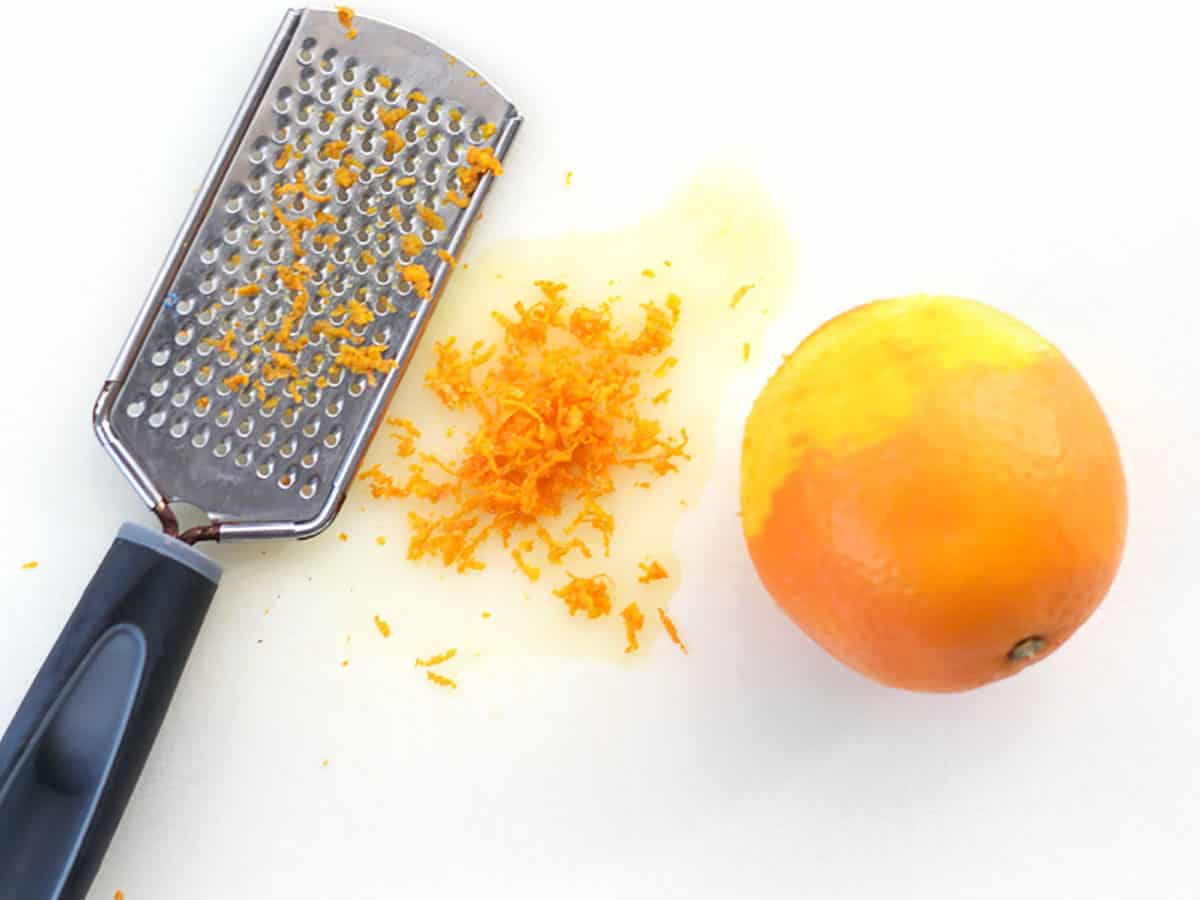 An orange that has been zested on a cutting board with a zester.