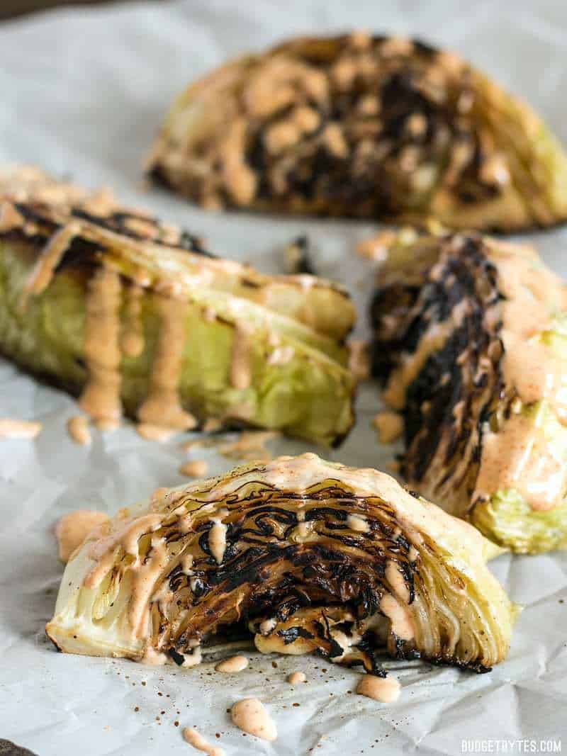 Wedges of Blackened Cabbage on parchment with chipotle sauce drizzled over top