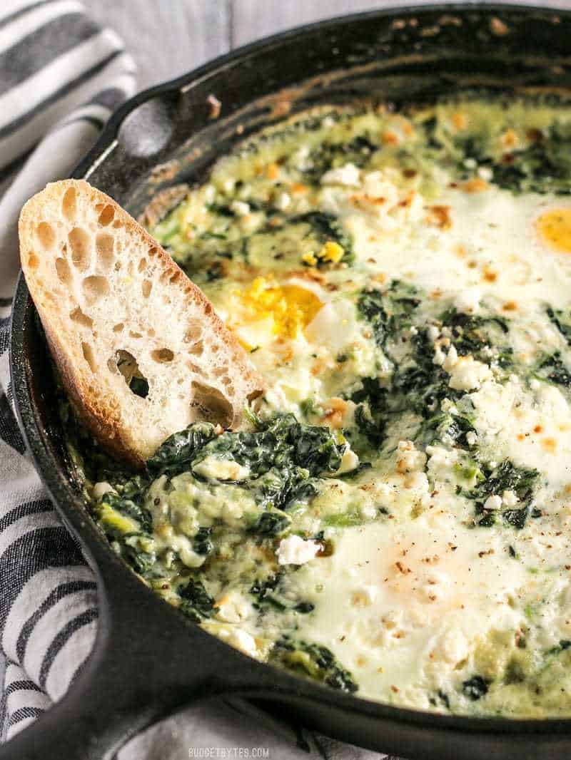 Creamed Spinach Baked Eggs in a cast iron skillet with a piece of bread dipped in