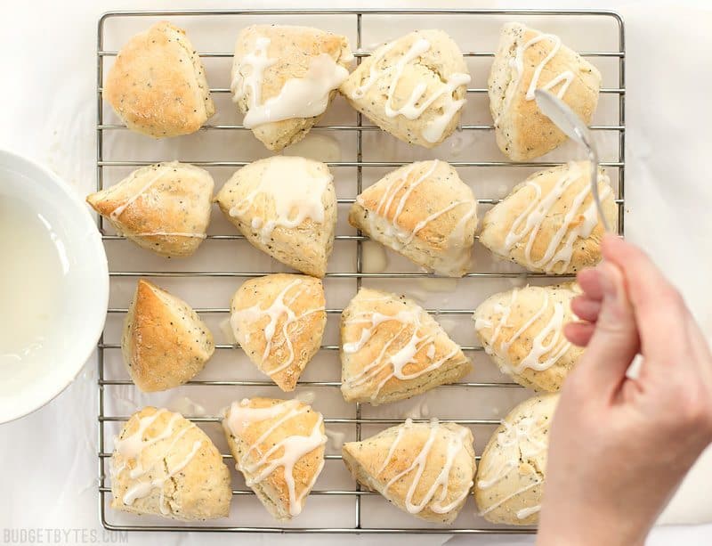 Lemon glaze being drizzled over lemon poppy seed two-bite scones on a wire cooling rack