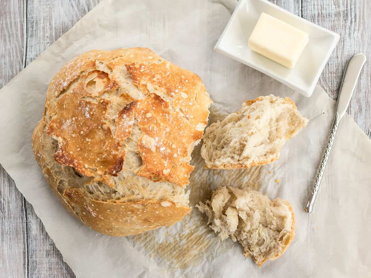 Overhead view of a loaf of no-knead bread on parchment with butter on the side. 