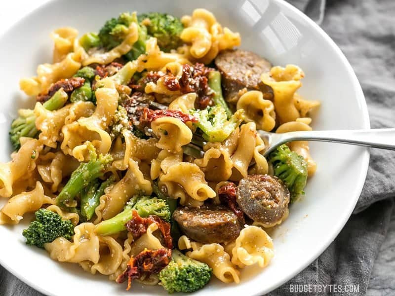 Close up of a bowl full of One Pot Sausage and Sun Dried Tomato Pasta with a fork in the side