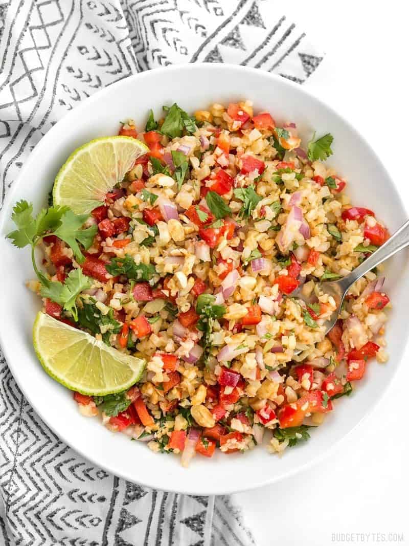 Peanut Lime Cauliflower Salad in a bowl, garnished with lime wedges and cilantro leaves