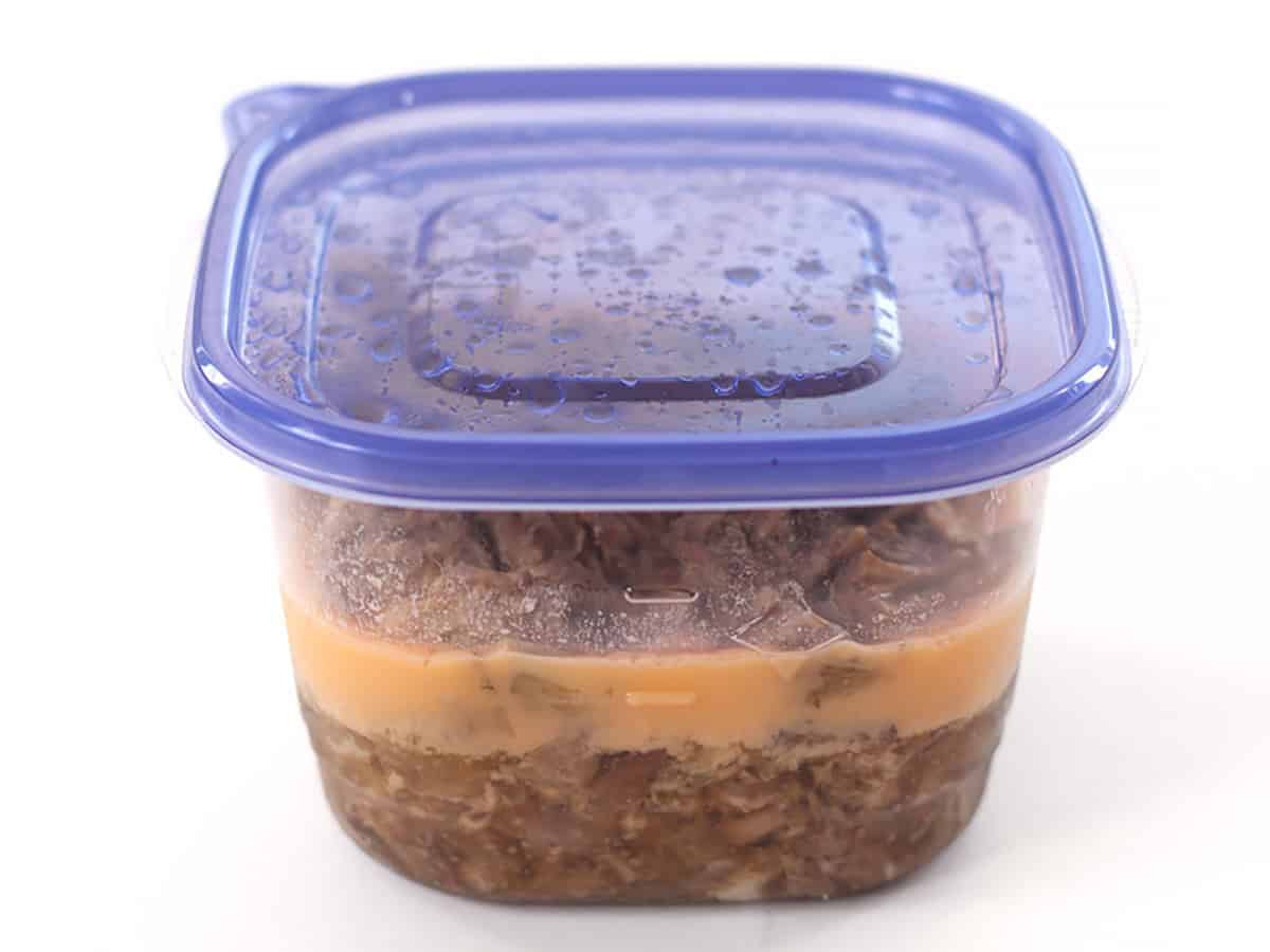 Cooked carnitas meat and juices in a food storage container.