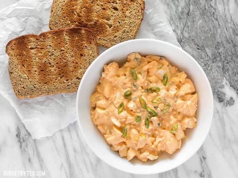 A bowl of Sriracha Egg Salad next to two slices of toast