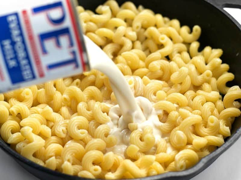 Evaporated Milk being poured onto cooked pasta in the cast iron skillet