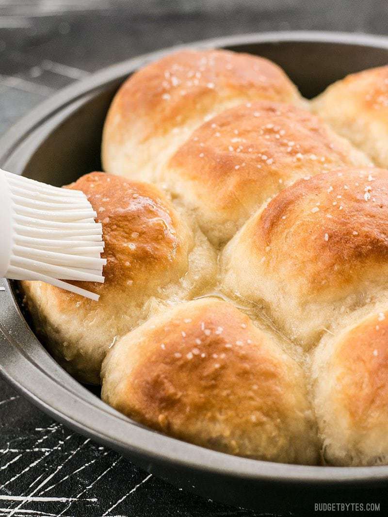 Melted butter being brushed onto Buttermilk Pull-Apart Rolls in the baking pan