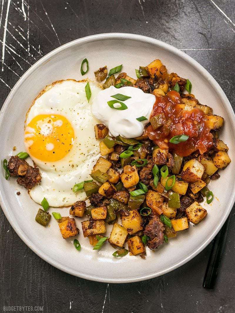 A plate full of Chorizo Breakfast Hash with a sunny side up egg, a dollop of sour cream, and salsa